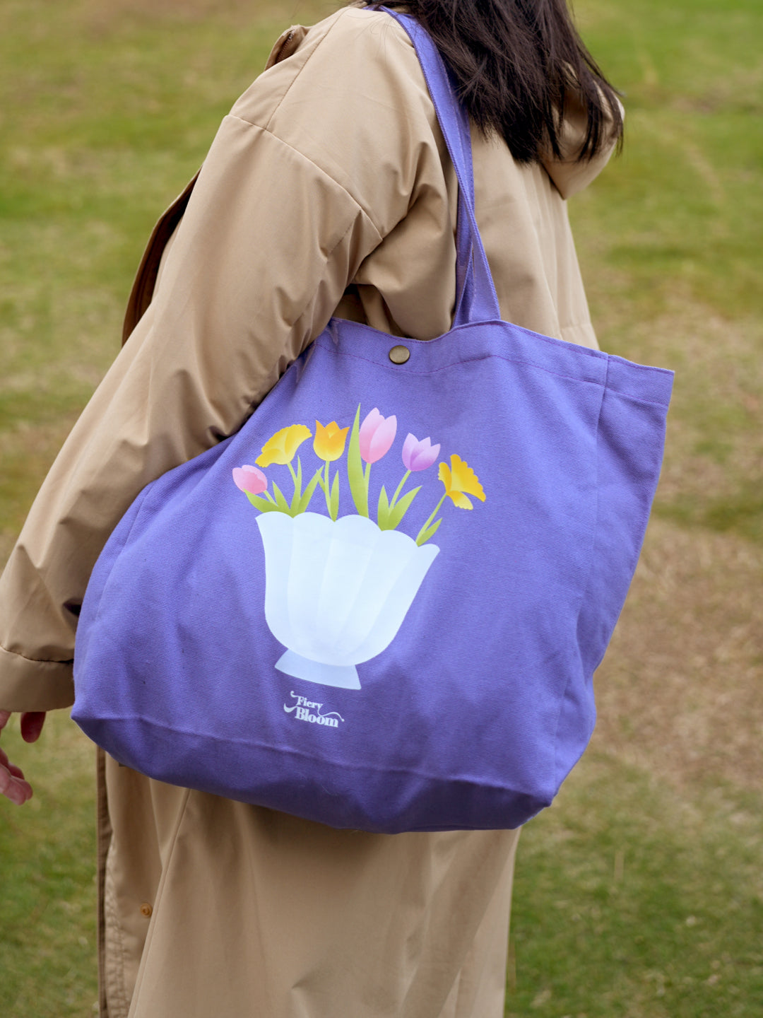 A person carrying a purple floral tote bag filled with fresh produce at a farmers market.